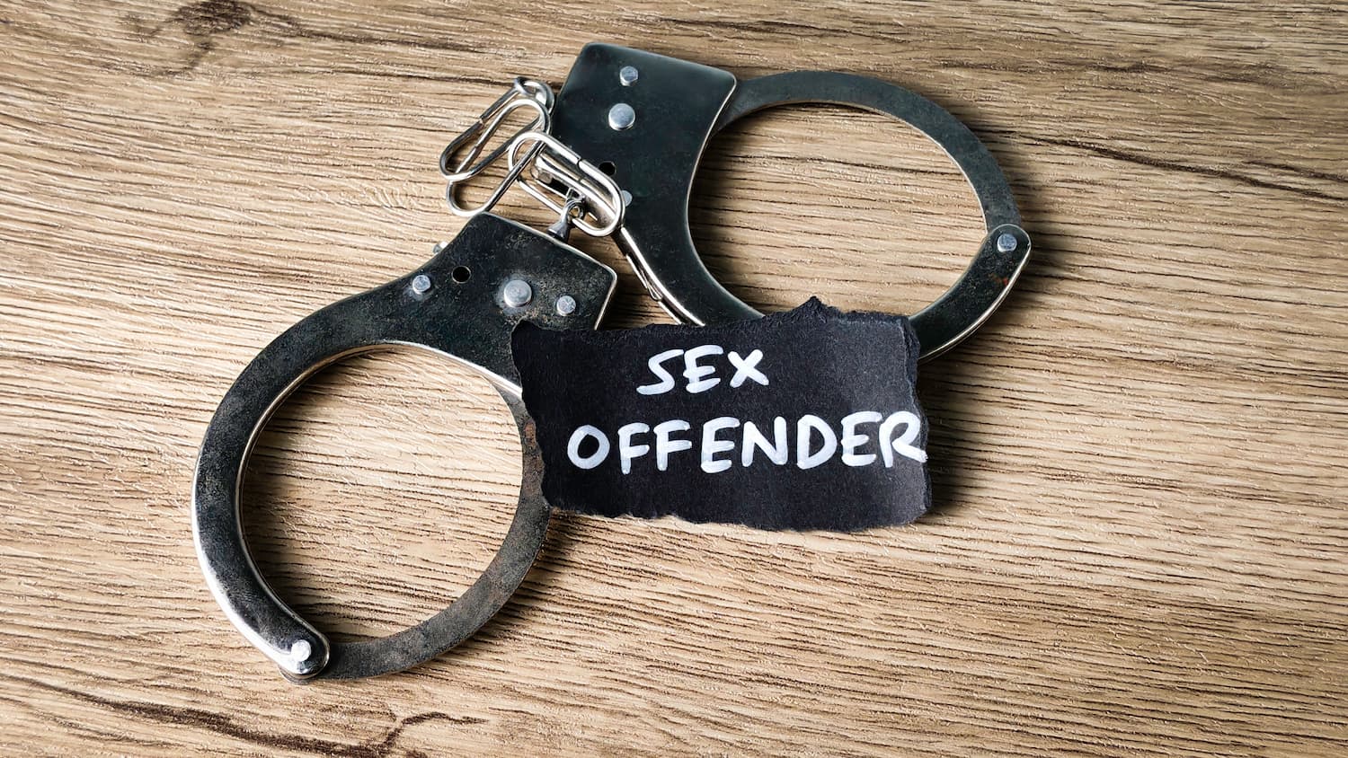 Sex offender concept with handcuffs on wooden surface representing sex crime arrest and legal consequences
